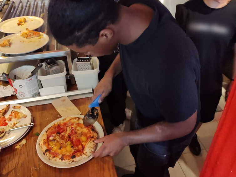 Un joven corta la pizza ya elaborada