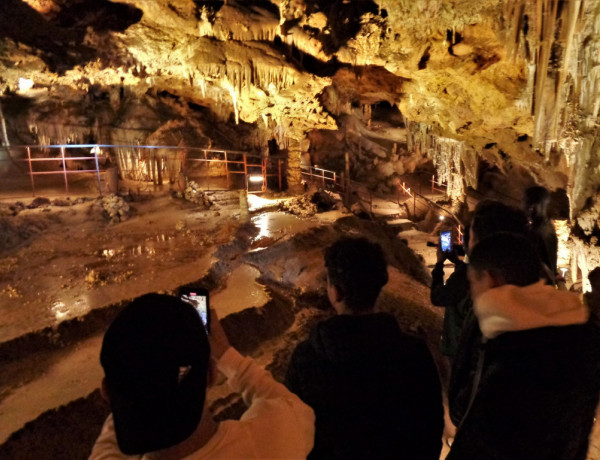 Tres jóvenes hacen fotos con sus móviles a las estalactitas en una de las cámaras de la cueva