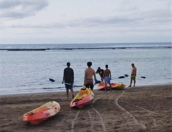 Tres menores preparan sus kayaks en la orilla del mar junto a una monitora y un educador