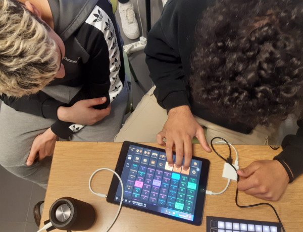 Dos jóvenes manejan la mesa de mezclas y la tablet para componer un tema