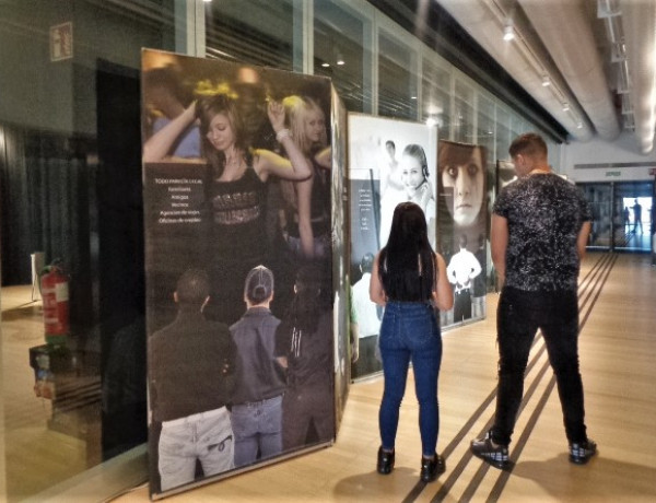 Una chica y un chico posan de espaldas junto a varios de los paneles de la exposición