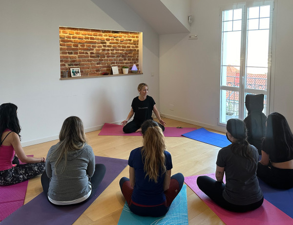 Seis mujeres realizan uno de los ejercicios de yoga guiadas por la monitora del taller