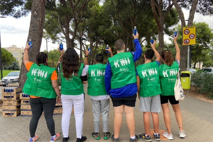 Jóvenes voluntarios en el Circuito RunCáncer 2022 levantan botellas de agua de las que reparten a los corredores