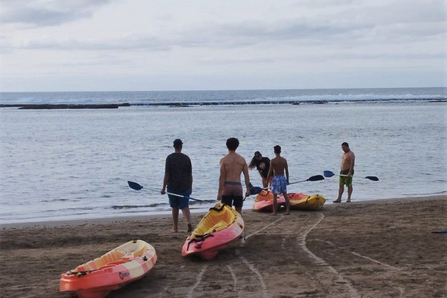 Tres menores preparan sus kayaks en la orilla del mar junto a una monitora y un educador