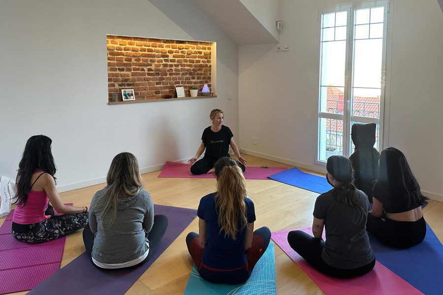 Seis mujeres realizan uno de los ejercicios de yoga guiadas por la monitora del taller